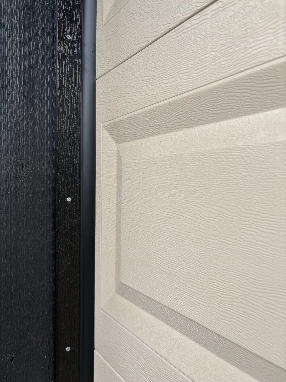 Close-up of vinyl weather stop installation with screws visible on black garage door frame